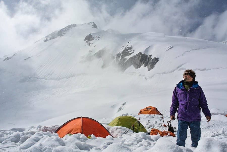 Muž stojaci vedľa stanov v snehu v horách